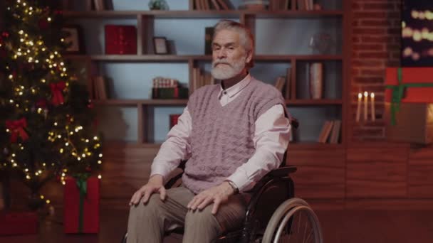 坐在轮椅上微笑的老人 坐在装饰过的客厅里 背景是除夕夜 在养老院的老年残疾祖父 寒假与残疾人概念 — 图库视频影像