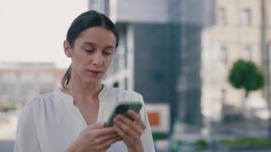 Gülümseyen İş kadını Modern Ofis Binası 'nın yanında duran akıllı telefonu kullanıyor. Akıllı Telefon Ekranı 'na Bakan ve Mutlu Hisseden Kadın. 