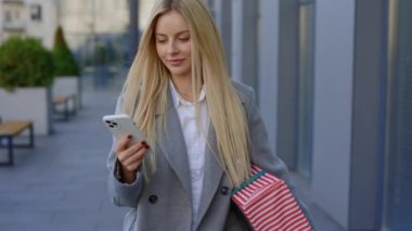 Sarışın Çekici Kadın İş Sokağında yürüyor, hediye kutusunu taşıyor ve akıllı telefon kullanıyor. Genç ve güzel bayan, cep telefonunda arkadaşlarıyla mesajlaşıp sohbet ediyor.