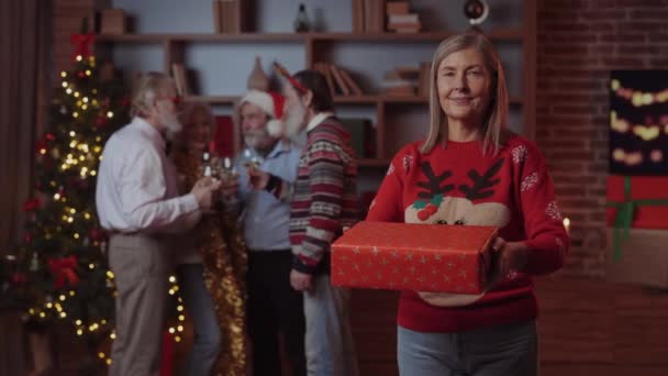Oudere Aantrekkelijke Dame Geeft Nieuwjaarscadeau Aan Camera Terwijl Haar Familieleden — Stockvideo