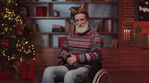 お祝いのムードでポジティブな高齢者男性は クリスマスハウスの装飾された車椅子に座っています 障害者 ハッピー ベアード ホーム お祝い — ストック動画