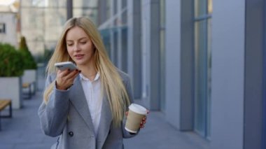 Ofis binası yakınlarında yürüyen bir iş kadını müşterilerine sesli mesaj kaydediyor. Kafkas Sarışın Kadın, Smartphone Ses Tanıma, Dikte Ediyor. İş ve Teknoloji Konsepti