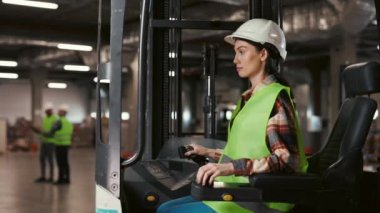 Forklift 'te oturan ve kameraya gülümseyen güzel depo işçisi kadının portresi. Kameraya bakan olumlu sürücü, Büyük Endüstriyel Depo 'da çalışıyor.