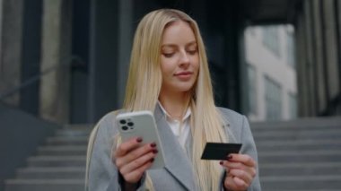 İçerik Genç Sarışın Kadın Dışarıda Duruyor, İnternetten Alışveriş İçin Akıllı Telefon ve Kredi Kartı Kullanıyor, Moda Giysileri veya Faturaları Ödemek için E-Ticaret İşlemleri Yapıyor