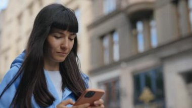 Şehir caddesinde yürürken, günlük kıyafetlerle akıllı telefon kullanan beyaz kadının yan görüntüsü. Dışarıdaki sevimli kadın telefon kullanıcısı. Arkadaşlarla mesajlaşmak. Çekici Kız Kaydırma Uygulamaları