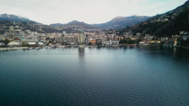 湖上的空中景观和海滨的卢加诺镇 靠近水的城市和背景中的阿尔卑斯山的无人机 旅游及旅游概念 — 图库视频影像