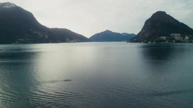 Lugano ve Alp Dağları 'nın havadan görünüşü. İnsanlar kanoya biniyor. İsviçre, İHA olarak doğruca Lugano Gölü 'nün üzerinde uçuyor. Seyahat ve Turizm Konsepti