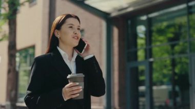 Resmi takım elbiseli gülümseyen iş kadını iş merkezinin yakınına gidiyor ve müşterileri elinde kahve fincanıyla telefonda konuşuyor. İnsanlar ve teknoloji kavramı