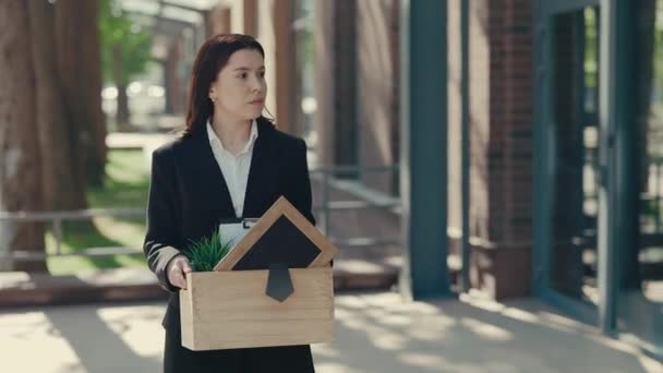 釈放されたばかりの仕事のない女性で ビジネスセンターの近くに行き 残念ながら仕事のアイテムを含む箱を持っているのを見ています 無関係な人々の概念 — ストック動画