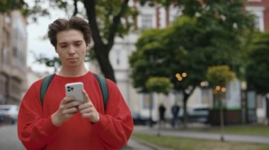Şehir caddesinde yürürken akıllı telefon kullanan, günlük kıyafetler içindeki yakışıklı beyaz adam. Dışarıdaki adam. Arkadaşlarla mesajlaşmak. Çekici erkek kaydırma uygulamaları. Teknoloji Konsepti