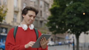 Beyaz adam Dijital Tablet kullanarak caddede dikiliyor. Dışarıdaki yakışıklı adam kullanıcısı. Erkek Turist Kaydırma ve Ekrana Bakma, İnternete Bakma, Sohbet. Halk ve Teknoloji Konsepti