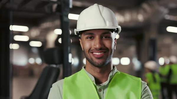 Multi-Ethnic Man Worker in Protective Yellow Vest Looking at Camera. Engineer Standing and Posing with Crossed Arms in Background in the Plant of Factory