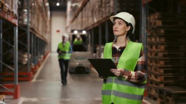 Bayan Depo Yöneticisi, Yoğun Nakliye Merkezi 'nde Envanter Denetlemesi Yapıyor. Modern Depolama Tesisleri 'ndeki operasyonları denetliyorum. Miğferli İşçiler Depo 'da İşbirliği Yapıyor