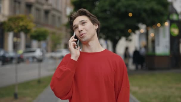 笑顔の若者が通りを歩き 屋外で電話で話している 学生は外でスマートフォンを使用しながら元気そうに見える — ストック動画