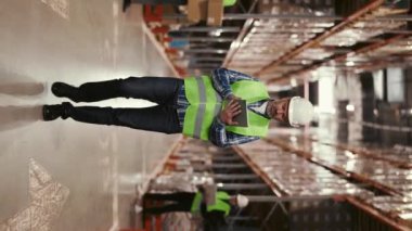 Dikey video. Güvenli Giyimde Olgun İşçi Perakende Deposunda Dijital Tablet ile Stokları Kontrol Ediyor. Lojistik ve İkmal Merkezi Operasyonları. Lojistik ve İkmal Merkezi 'nde çalışıyorum.