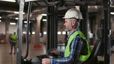 Forklift kamyonunda oturan Olgun Adam Depo işçisi. Neşeli Adam Endüstriyel Kamyon Çalıştırıyor, Kameraya Gülümsüyor. Büyük Endüstriyel Depo 'da Mutlu Forklift Şoförü