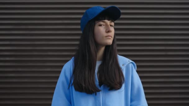 一位严肃的年轻女子 棕色头发 头戴蓝色帽子 穿着休闲装 站在城市街道上 这张户外肖像画描绘了她在城市中的观光客或旅行者 — 图库视频影像
