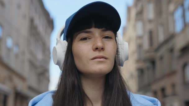 カメラを眺めながらヘッドフォン付きのトランキルレディ 路上でワイヤレスイヤホンを見つけず 音楽の音を味わった女性 人とモダンなテクノロジーの融合 — ストック動画