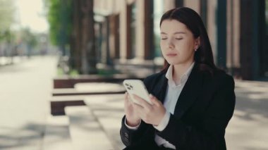 Kafkasyalı iş kadını merdivenlerde oturuyor ve akıllı telefonu iş için kullanıyor. Resmi takım elbiseli bir kadın telefon kullanıyor, iş uygulamalarını çalıyor. Kapat.