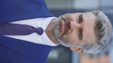 Dikey video. Yakışıklı Sakallı Olgun İş Adamı Kamerada Gülümseyen Açık Hava, Çapraz Eller. Dışarıdaki Şık Kıyafetler Giyen Pozitif Patron 'un Portresi. Kapat.
