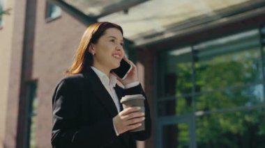Resmi takım elbiseli Kafkasyalı iş kadını iş merkezinin yakınına gidiyor ve elinde kahve bardağı olan müşterilerle telefonda konuşuyor. İnsanlar ve teknoloji kavramı