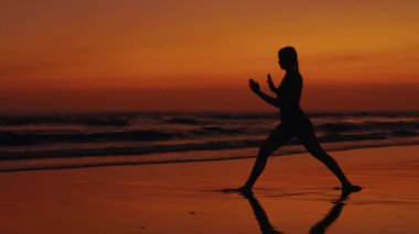 Gün batımında Yoga Yapan Sporcu Kadın 'ın silueti. Sıska Kız deniz kıyısında antrenman yapıyor. Dışarıda esneyen atletik kadın. Yoga ve İnsanlar Konsepti