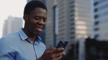 Mutlu Afro-Amerikan Yöneticisi Dışarıda Duruyor ve telefonunda internet geziyor. Gülümseyen İşadamı Açık Hava 'da Mobile' daki videoyu izliyor. Halk ve Teknoloji Konsepti