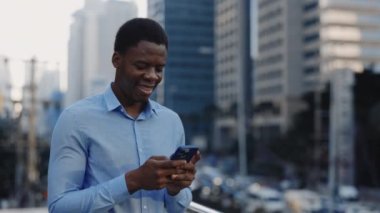 Yakışıklı Çalışan İş Bölgesi 'nde duruyor ve müşterilerle mesajlaşıyor. Açık havada akıllı telefonuyla konuşan Afro-Amerikalı genç iş adamı. Halk ve Teknoloji Konsepti