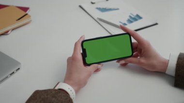 Genç Kadın Eller Yatay Tutma Akıllı Telefonu ile Chroma Anahtarı. İş kadını yeşil ekranlı cep telefonundan video izliyor. Ofis, Chroma Key. Yeşil Ekran Konsepti