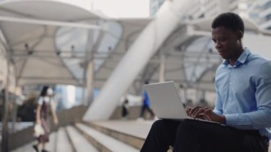 Yakışıklı Pozitif Adam Uzaktan Kumandası 'nın yan görüntüsü dışarıda otururken laptopta çalışıyor. Afrika kökenli Amerikalı Dışarıda İşçi Bilgisayarda Kod Yazıyor. Halk ve Teknoloji Konsepti
