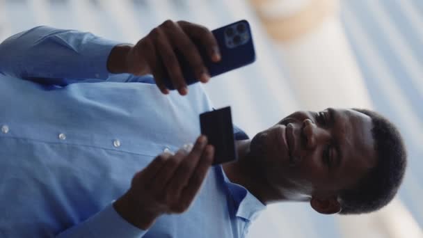 垂直ビデオ スマートフォンでオンラインで支払うハンサムなアフリカ系アメリカ人の男 銀行カード番号を追加 外に立っています 電話でオンラインで購入する多民族男性 ショッピング モバイル決済コンセプト — ストック動画