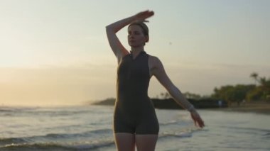 Sarışın, sevimli sporcu kadın antrenmandan önce kaslarını esnetiyor. Kasları ısıtan kız deniz kenarında aerobik yapıyor. Fiziksel Eğitim Konsepti