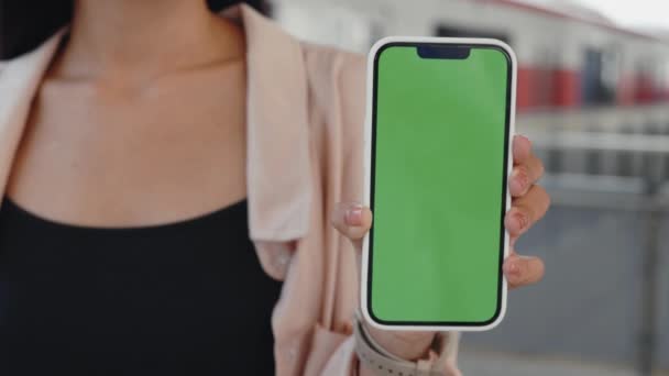 地下鉄駅の背景に緑色のスマートフォンを持っている女性 クロムキーのカメラに表示する彼女の手の電話を持つ観光客 クローズアップ トラベル テクノロジーコンセプト — ストック動画