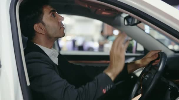ハッピーな男性オーナーが新車をチェック ハンサムな若いビジネスマンがサロンで車を買って周りを見回した 人と車のディーラーのコンセプト — ストック動画