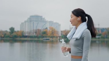 Koşarken ya da egzersiz yaparken şişeden su içen kadın. Esmer Asyalı kız koşudan ya da egzersizden sonra temiz maden suyu içer. Açık havada Antrenman