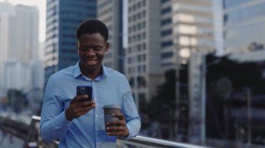 Pozitif Yakışıklı Satış elemanı müşterilerle sohbet ederken dışarıda dolaşıyor ve kahve içiyor. Modern İşadamı Ofise Gidiyor, Kahve molasında Akıllı Telefon kullanıyor. Halk ve Teknoloji Konsepti