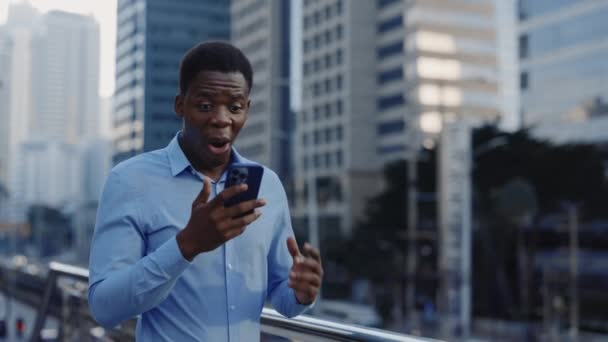 快乐的非洲裔美国人在情感上庆祝成功和好消息 商人站在办公大楼附近 用他的智能手机庆祝胜利 — 图库视频影像