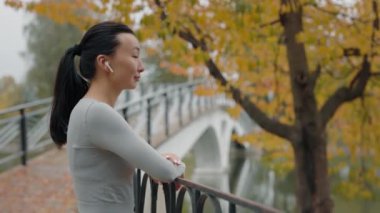 Asyalı Kadın Koşucunun Dışarda Müzik Dinlerken Görünüşü. Koşu yaptıktan sonra sonbahar parkında dinlenen koşucu kadın. Atletik Sporcu Kadın Koşu. Spor ve Sağlıklı Yaşam Biçimi