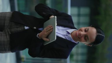 Dikey video. Gülümseyen Şirin İş Kadını Uzaktan Çalışmak İçin Tablet Kullanıyor, Sohbet Ediyor. Dışarıda durup Gadget 'ta video izleyen mutlu kadın ofis çalışanları. Halk ve Teknoloji Konsepti