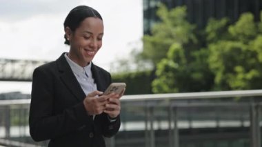 Gülümseyen Kadın Danışmanlığı Çevrimiçi, dışarıda yürürken akıllı telefon kullanıyor. Genç Mutlu Girişimci İş Merkezi 'ne gidip İş Grubu Sohbetinde Sohbet Ediyor