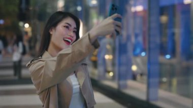 Asyalı Güzel Kadın Harika Gece Şehir Manzarası 'nda Selfie Çekiyor. Cep telefonu kullanan şık Asyalı kız kendini dışarı çıkartıyor. Halk ve Teknoloji