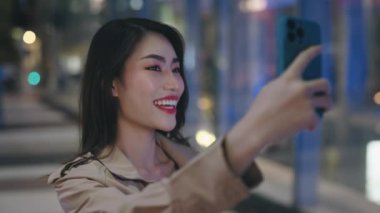 Neşeli Trans Kadın Gece Işıkları Arkaplanındaki Telefon Kamerasında Poz Veriyor. Çekici Bayan Açık havada Selfie Çekiyor ve Akıllı Telefon Kullanarak Gülümsüyor. Halk ve Teknoloji