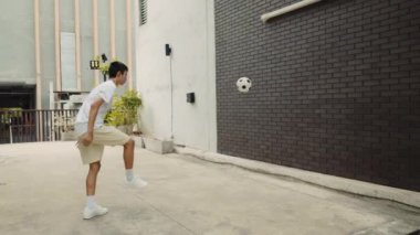 Genç Asyalı futbolcu duvardaki maçtan önce tekme pratiği yapıyor. Futbol oynamak için dışarıda sportif çocuk antrenmanı. Futbol ve İnsanlar Konsepti