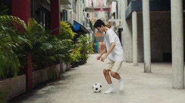 Boş Şehir Caddesinde futbol oynayan genç çocuk. Dışarıda koşan ve futbol oynayan yetenekli Asyalı genç adam. Çocukluk, spor. Futbol ve İnsanlar Konsepti