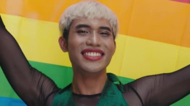 Genç Asyalı Transseksüel Adam ayakta duruyor ve LGBT topluluğunu kameraya gösteriyor. Boyalı Dudaklı, Güzel Giyimli Adam ve Gökkuşağı Bayraklı Makyaj Dışarısı Pozu. Çeşitlilik LGBT Kavramı