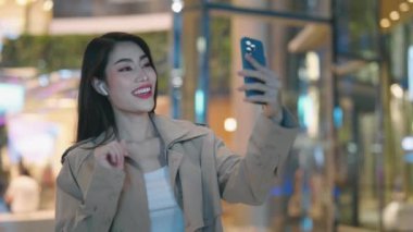 Gülümseyen Çekici Kız Turist Gece Kenti 'nde dikilirken görüntülü konuşma yapıyor. Şehirdeki Genç Bayan Turist Cep Telefonu Kullanıyor, Çevrimiçi Toplantı Yapıyor. Halk ve Teknoloji Konsepti