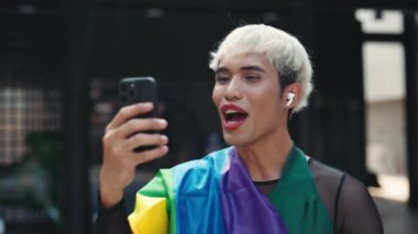 Gülümseyen Adam dışarıda duruyor ve arkadaşlarıyla video görüşmesi yapıyor. Dışarıdaki Yakışıklı Transseksüel Adam Geçit Töreni 'nden Aileleri Arıyor. LGBT ve Teknoloji Konsepti