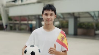 İspanyol Futbol Takımı 'nın Asya taraftarı, İspanyol Bayrağı ve Futbol Topu' nu tutuyor. Top ve Bayrak Poz Veren Yakışıklı Genç Adam, Kamerayı Arıyor. Futbol ve İnsanlar Konsepti