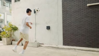 Asyalı erkek antrenman baş tekmesi, futbolda yeteneklerini geliştirir. Sokakta Maçtan Önce Genç Bir Futbolcunun Eğitimi. Futbol ve İnsanlar Konsepti