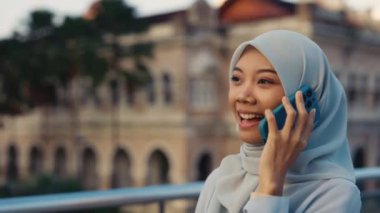 Sokakta yürüyen ve cep telefonuyla konuşan İslami Genç Kız. Mutlu Müslüman bayan dışarı çıkıyor ve akıllı telefonuyla arkadaşlarıyla konuşuyor. Halk ve Teknoloji Konsepti